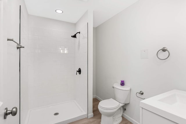 full bathroom with baseboards, toilet, wood finished floors, and a tile shower