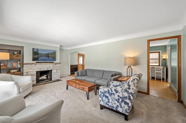 carpeted living room featuring a fireplace, arched walkways, baseboard heating, and baseboards