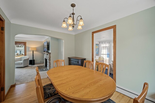 dining room featuring light wood-type flooring, a baseboard heating unit, arched walkways, and a fireplace