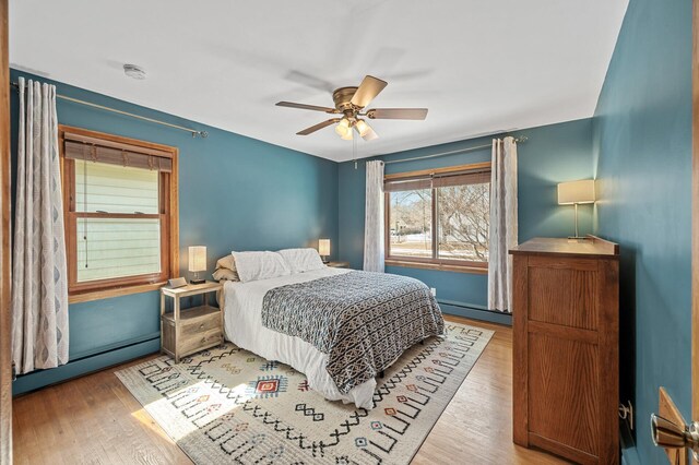 bedroom featuring a baseboard heating unit, wood finished floors, baseboard heating, and a ceiling fan