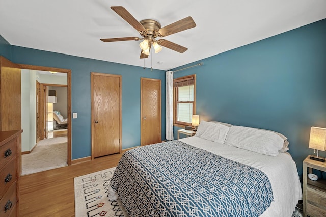 bedroom featuring baseboards, a ceiling fan, multiple closets, and wood finished floors