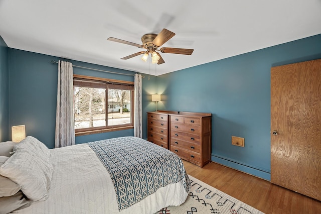 bedroom with wood finished floors, ceiling fan, and a baseboard radiator