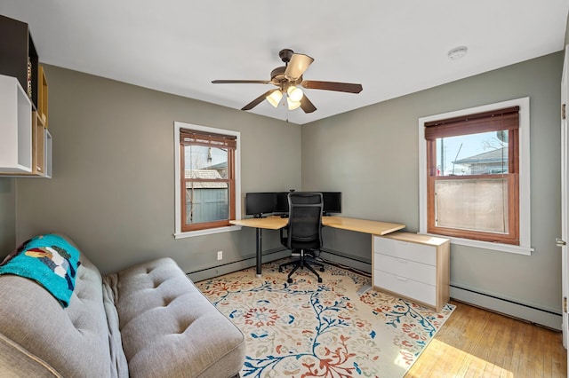 office space with a wealth of natural light, light wood-type flooring, baseboard heating, and a ceiling fan