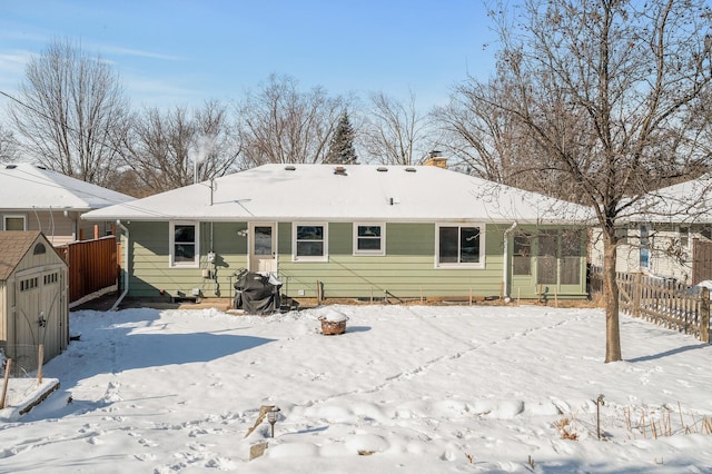 snow covered rear of property with an outbuilding, fence, a shed, and a chimney