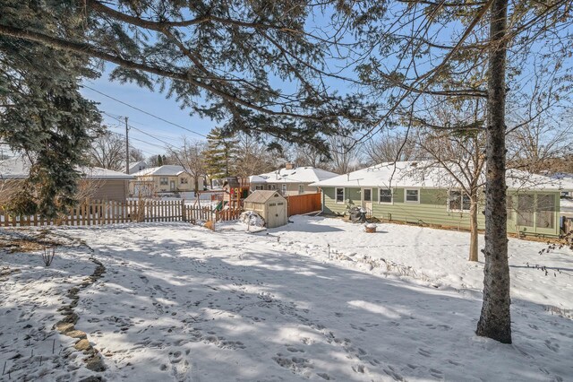 yard layered in snow with an outbuilding, a shed, a residential view, and fence