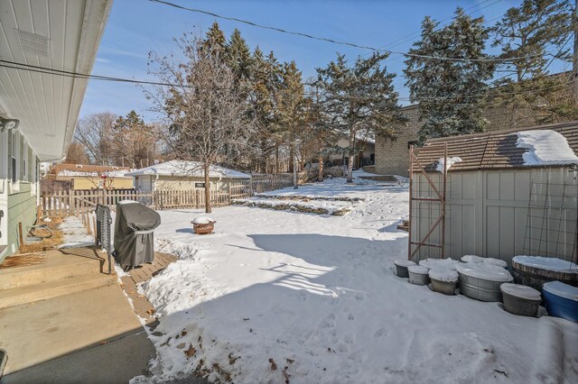 yard layered in snow featuring an outbuilding, a storage shed, and a fenced backyard