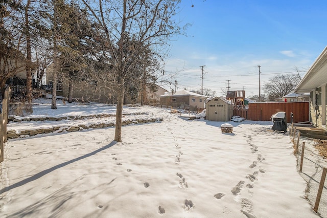 yard layered in snow featuring a shed, an outdoor structure, and fence