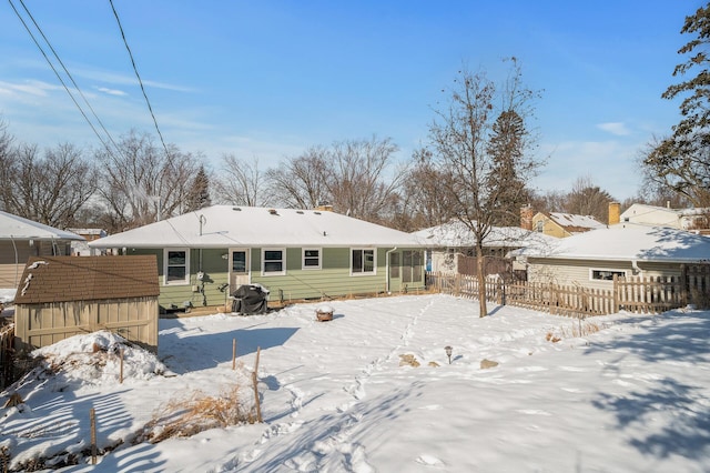 snow covered house featuring an outdoor structure and fence