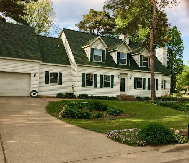 new england style home featuring a shingled roof, concrete driveway, a front yard, an attached garage, and a chimney