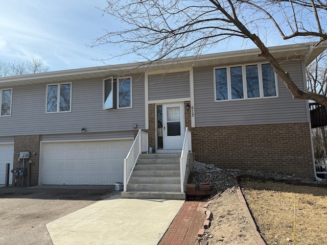 raised ranch featuring entry steps, a garage, brick siding, and driveway