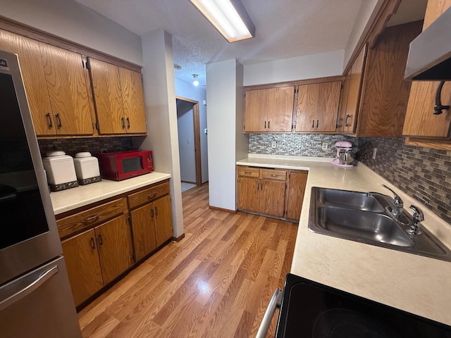 kitchen with a sink, light countertops, fridge, wall chimney range hood, and brown cabinets