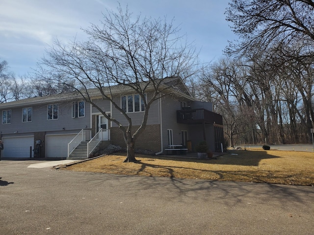 bi-level home featuring aphalt driveway, an attached garage, brick siding, and a balcony