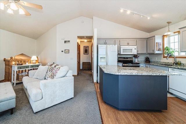 kitchen with a kitchen island, light stone counters, hanging light fixtures, white appliances, and a sink