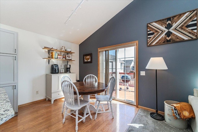 dining area with track lighting, light wood-style flooring, baseboards, and lofted ceiling