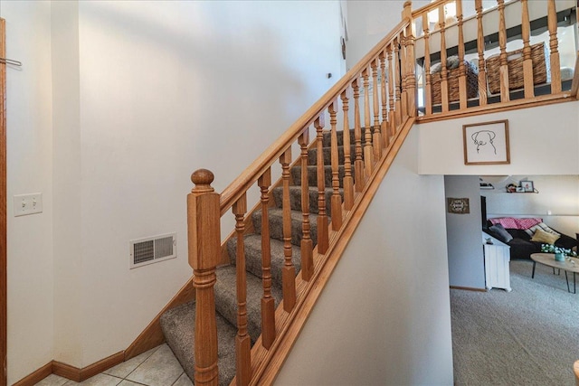 staircase with tile patterned floors, visible vents, carpet floors, a high ceiling, and baseboards