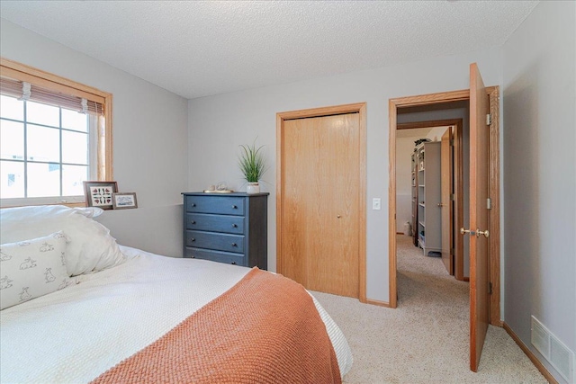 bedroom with visible vents, baseboards, light carpet, a closet, and a textured ceiling