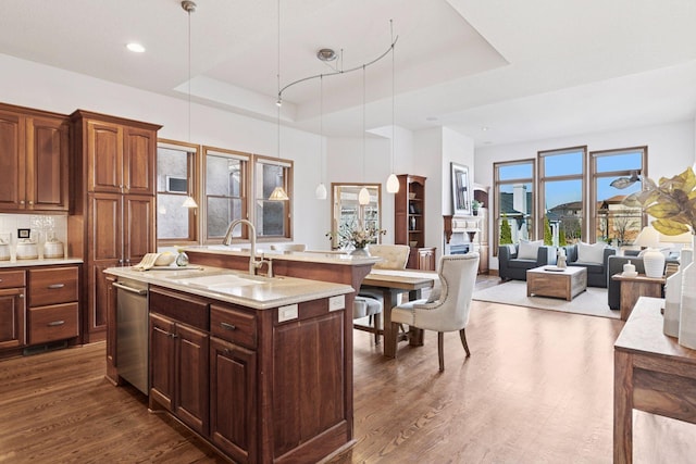 kitchen with dark wood-type flooring, a center island with sink, dishwasher, a raised ceiling, and a sink