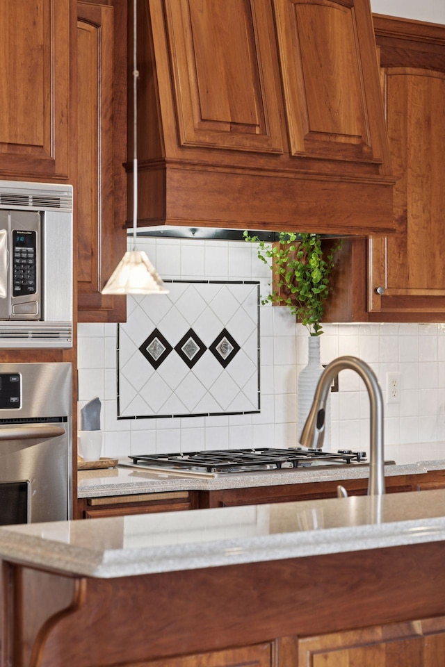 kitchen with light stone counters, decorative backsplash, appliances with stainless steel finishes, and brown cabinetry