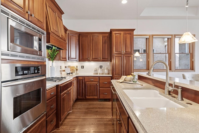 kitchen featuring dark wood-style floors, a sink, hanging light fixtures, stainless steel appliances, and backsplash