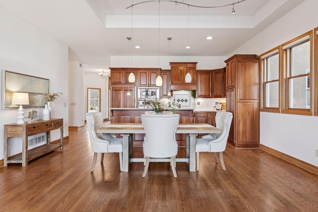 dining space with a raised ceiling, dark wood-type flooring, track lighting, recessed lighting, and baseboards