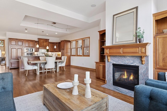 living room with a tray ceiling, baseboards, dark wood-style floors, and a fireplace