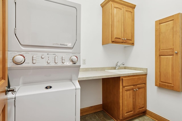 laundry room featuring cabinet space, stacked washer / drying machine, baseboards, and a sink