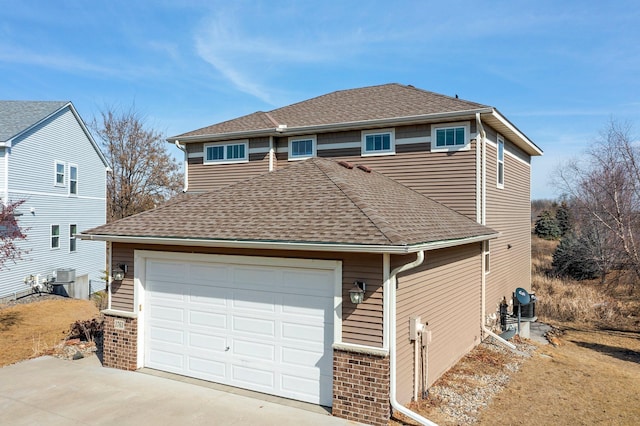 traditional home featuring brick siding, a shingled roof, concrete driveway, central AC unit, and a garage