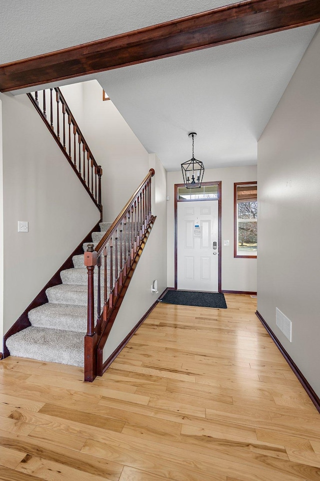 foyer featuring visible vents, baseboards, light wood-style flooring, and stairs