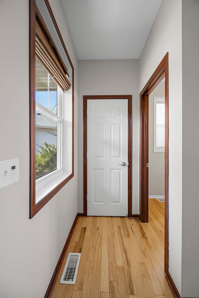 corridor with light wood-style flooring, baseboards, and visible vents