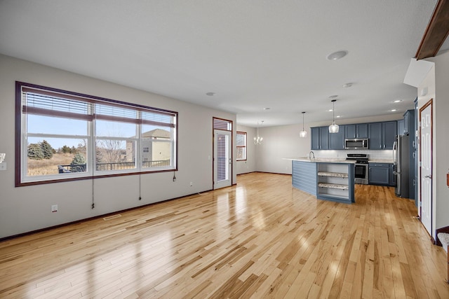 kitchen with decorative light fixtures, light countertops, light wood-style flooring, a notable chandelier, and stainless steel appliances