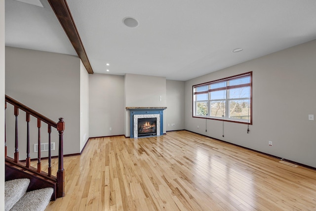 unfurnished living room featuring a glass covered fireplace, stairway, visible vents, and wood-type flooring