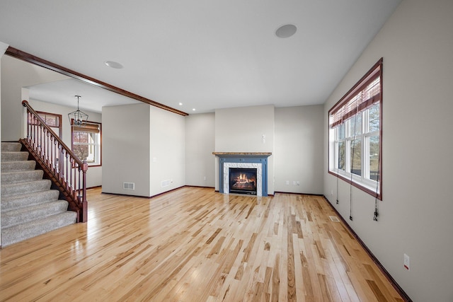 unfurnished living room featuring stairway, visible vents, light wood finished floors, an inviting chandelier, and a glass covered fireplace