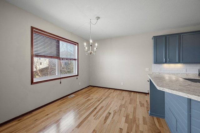 unfurnished dining area with visible vents, baseboards, a sink, light wood-type flooring, and a chandelier