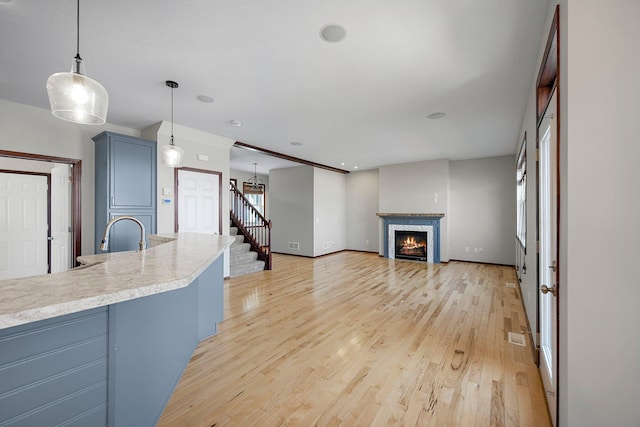 unfurnished living room featuring baseboards, a warm lit fireplace, a sink, stairs, and light wood-type flooring