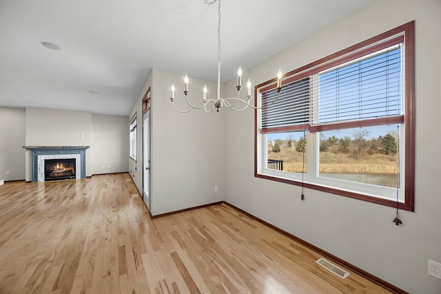 unfurnished dining area featuring visible vents, baseboards, a chandelier, light wood-type flooring, and a glass covered fireplace