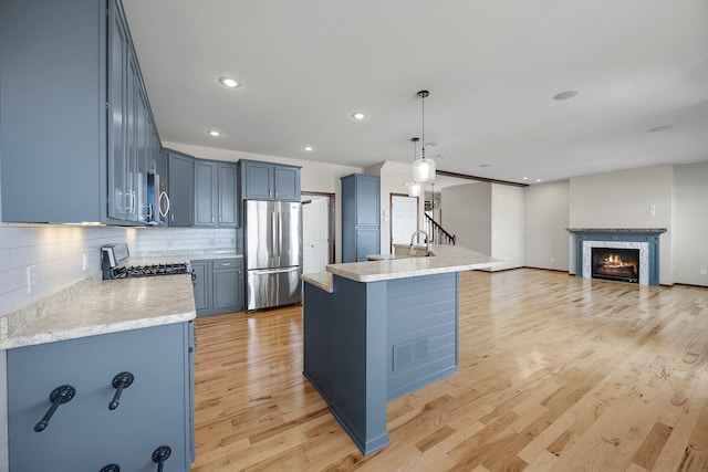 kitchen with blue cabinets, a lit fireplace, appliances with stainless steel finishes, light wood finished floors, and decorative backsplash