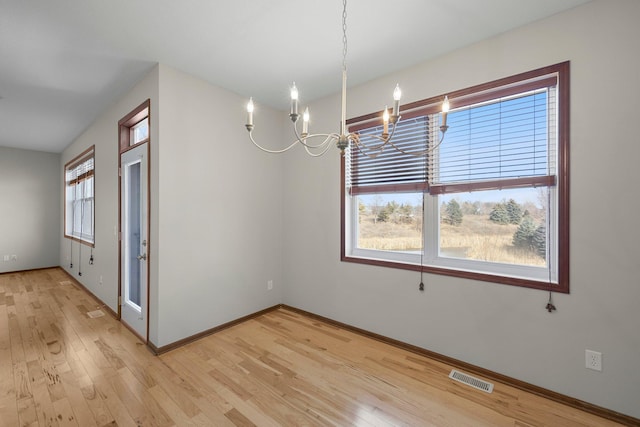 unfurnished dining area with light wood-type flooring, baseboards, visible vents, and a chandelier