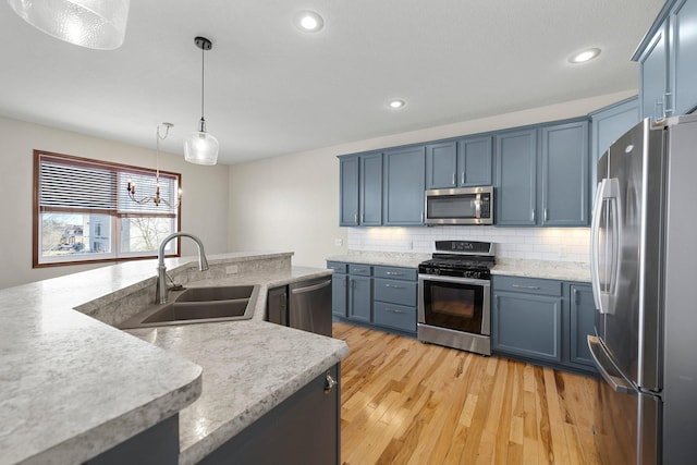 kitchen with blue cabinets, light wood-type flooring, a sink, appliances with stainless steel finishes, and decorative backsplash