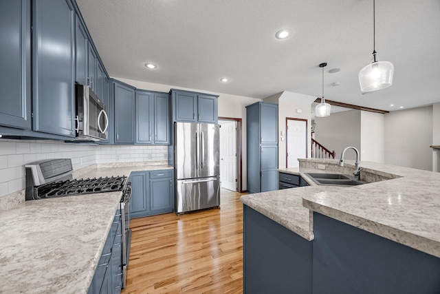 kitchen with blue cabinetry, appliances with stainless steel finishes, light countertops, and a sink