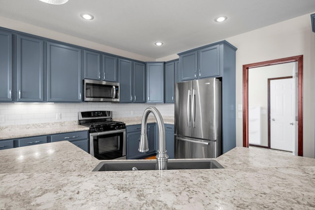 kitchen featuring a sink, stainless steel appliances, backsplash, and blue cabinets