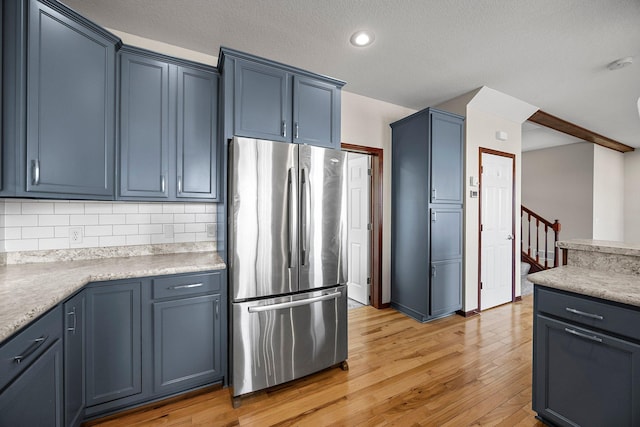 kitchen with blue cabinets, tasteful backsplash, light wood-style flooring, and freestanding refrigerator