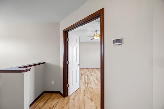 corridor with light wood-type flooring, baseboards, and an upstairs landing