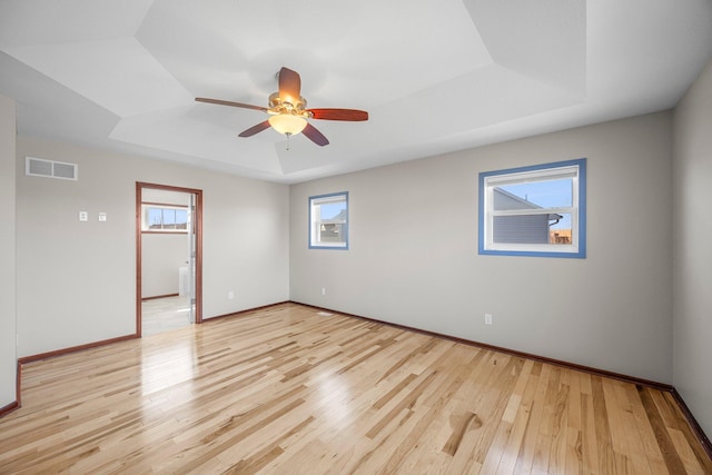 spare room with visible vents, light wood-style flooring, a tray ceiling, baseboards, and ceiling fan