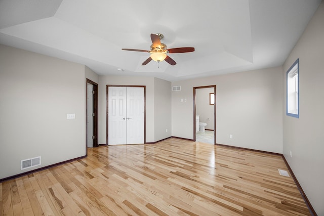 unfurnished bedroom featuring light wood finished floors, visible vents, baseboards, and a tray ceiling