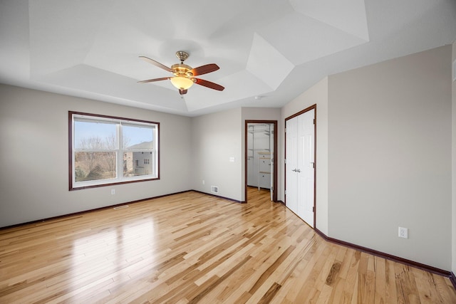 unfurnished bedroom with a tray ceiling, visible vents, baseboards, and light wood finished floors