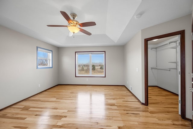 unfurnished bedroom with a raised ceiling, baseboards, light wood-type flooring, and ceiling fan