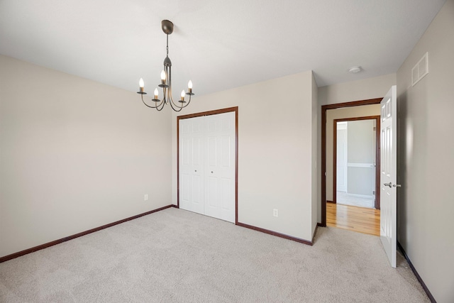 unfurnished bedroom with an inviting chandelier, light colored carpet, visible vents, and baseboards