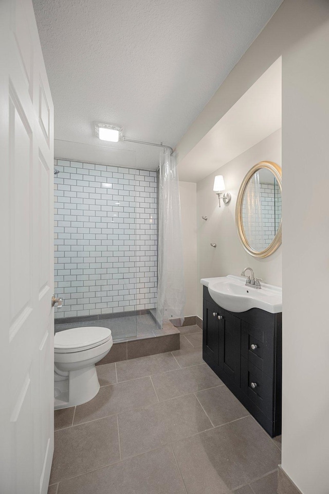 bathroom featuring tile patterned floors, toilet, a textured ceiling, a tile shower, and vanity