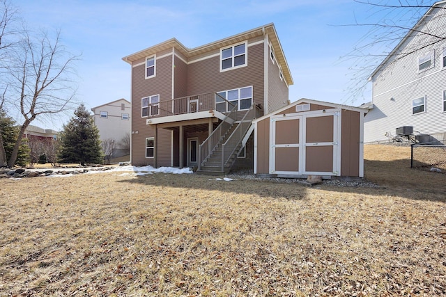 back of house featuring stairway, central AC unit, a lawn, a storage shed, and an outbuilding