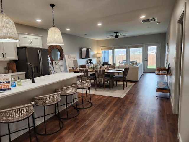 kitchen featuring visible vents, a kitchen breakfast bar, black fridge with ice dispenser, dark wood finished floors, and white cabinetry